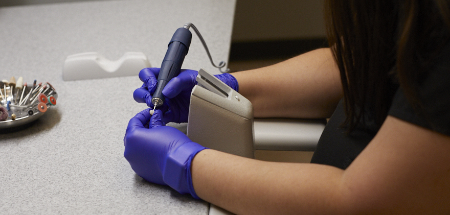 Gloved hands using a tool to make dental crown.