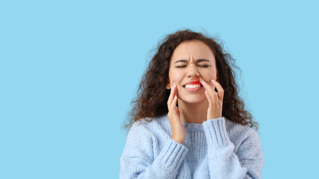 Woman with curly hair touching face near mouth in pain.