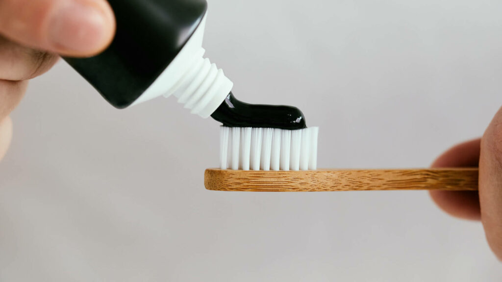 Close up of a hand squeezing charcoal toothpaste on a bamboo toothbrush.