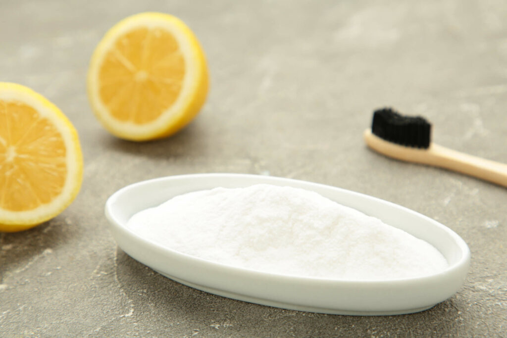 Wooden bamboo eco friendly toothbrush, baking soda, and lemon on grey background