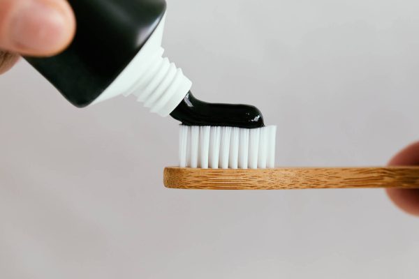 Close up of a hand squeezing charcoal toothpaste on a bamboo toothbrush.