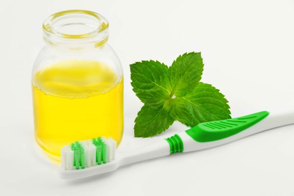 Jar of oil, mint leaf and green toothbrush with a white background.