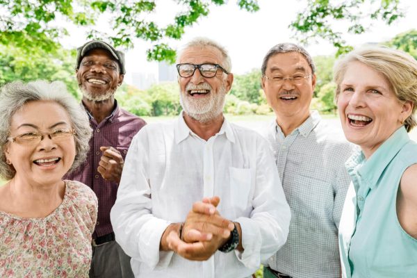 Group of diverse senior adults smiling and laughing outside underneath a tree on a sunny day.